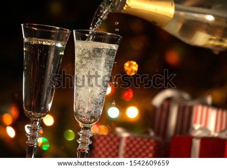Beautiful splash of champagne glasses and Christmas gifts on the background of Christmas lights