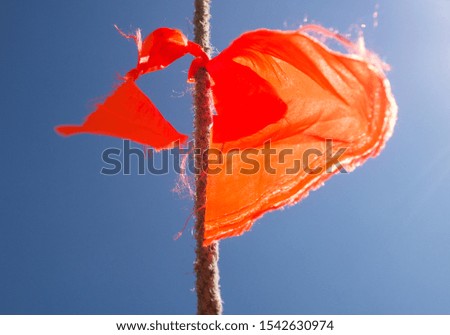 Low angle colour image of a frayed piece of orange bunting tied to a rope against a clear blue sky