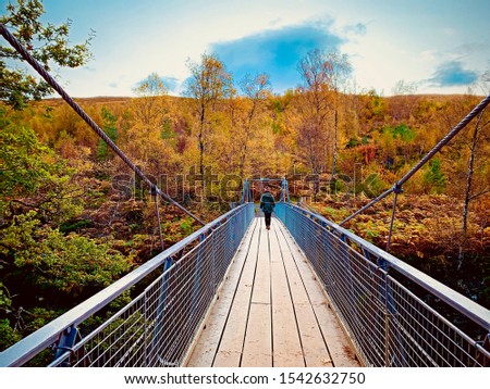 A young woman walks on a suspension bridge at Corrieshalloch Gorge in Scotland, with beautiful autumn colours.
