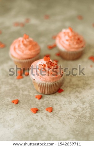 Pink cupcakes on a gray background for Valentine's day. Gift sweets with cream and sprinkle with hearts.