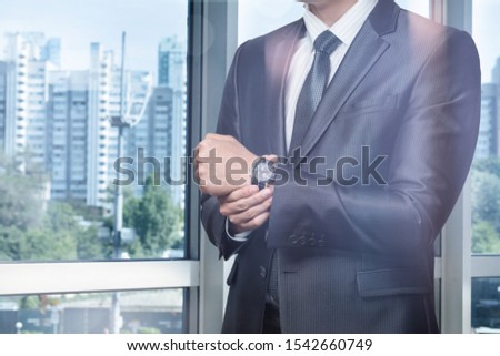 Young businessman corrects a wristwatch against the window overlooking the city.