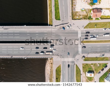 Photo of cross roads. Multi-lane roads pose a danger for people. On the left part bridge over water. Cars waiting for green signal of traffic light. Comfortable and convenient movement on your own car