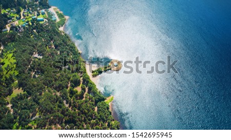 Picturesque aerial of the lake shore. Beautiful view from above to the green forest and lawns on the sandy bank, blue waves driven by the wind and shadows of clouds passing by.