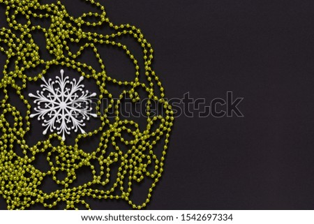 Holiday background , white snowflake and green bright decorative beads on black background, flat lay, top view