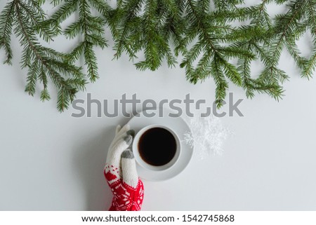 Female hands in the winter gloves with cup of black coffee and glowing snowflake in spruce branches on a white table. Christmas and New Year concept. Coffee art. Flat lay, top view. 