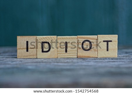 word idiot made of wooden letters on a gray table on a green background