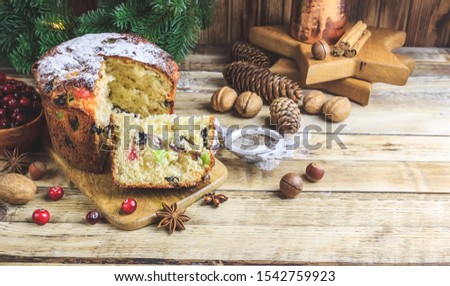 Traditional Christmas panettone with raisins and dried fruits on rustic wooden table. Christmas decorations, caramel canes, cinnamon, star anise, assorted nuts. Selective focus