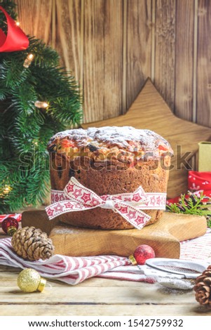Traditional Christmas panettone with raisins and dried fruits on rustic wooden table. Christmas decorations, caramel canes, cinnamon, star anise, assorted nuts. Selective focus