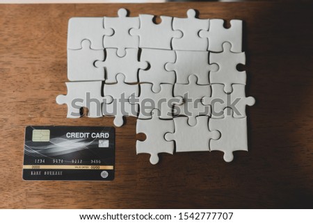 A white jigsaw puzzle on a brown wood floor and having a credit card idea / business team