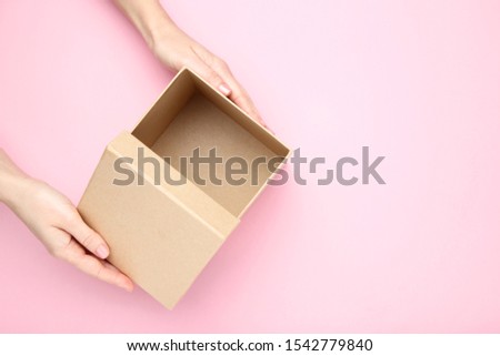 Female hands opening brown gift box on pink background