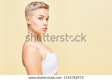 Natural beauty, youth, health and style concept. Side image of attractive blue eyed blonde young European female with stylish pixie hairdo having confident facial expression, looking at camera