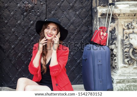 Smiling tourist woman is talking on cell phone near door. Travel adult girl speaks by smartphone near old door on the street.