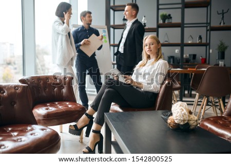 elegant awesome female boss sitting with laptop in hands, her co-workers havng a conversation in the background of the photo. lifestyle, job, profession, occupation