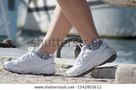 Women legs in white shoes sitting in the seaside in the sea port. Concept of journey travel or sport background. Royalty-Free Stock Photo #1542803612