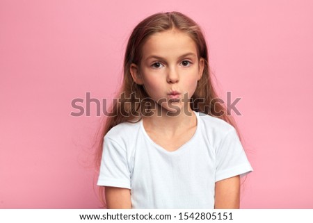 closeup portrait of serious little kid in white t-shirt with pursed lips and large eyes. kid staring at the camera . close up portrait, isolated pink background.