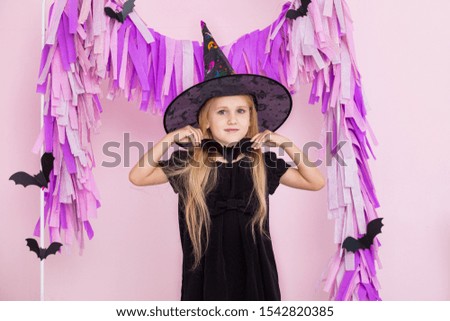 Little beautiful cute child girl in witch carnival costume in fashionable Halloween decorations