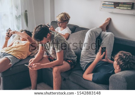 Group of teenager using smartphone sitting on a sofa at home. Young boys and a girl sharing photo and video watching social story online. Friends enjoying new trend technology. Youth and tech concept Royalty-Free Stock Photo #1542883148