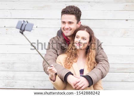 Young couple taking selfies in front of a wooden wall