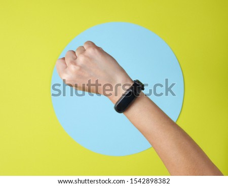 Smart bracelet on hand wrist on green background with blue circle. Top view