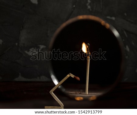 Broken match is against the mirror and the reflection shows a whole standing burning stick. Black background.