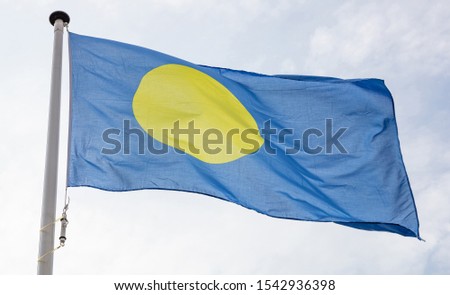 Palau flag. Palauan national sign and symbol waving on a flagpole against cloudy sky background