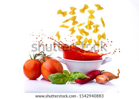 isolated from the white background, the raw Italian pasta in the shape of a butterfly falls into the pan with tomato sauce