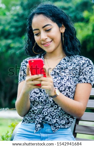 Colorful photo of a pretty young woman dressed in a black and white shirt with flowers, chatting with her smart phone. Concept of feminine beauty. Vertical image