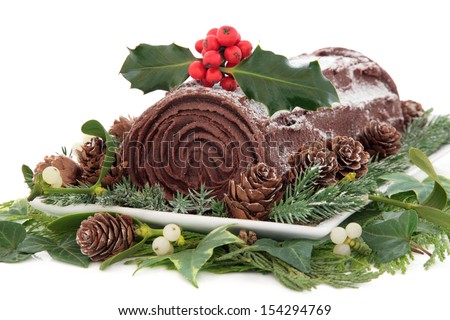 Christmas chocolate yule log cake with holly, mistletoe, snow, pine cones and winter greenery over white background. 