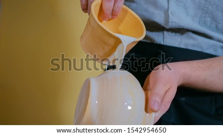 Professional male potter preparing ceramic wares for burning in pottery kiln with milk - old russian pottery tradition. Crafting, artwork and handmade concept Royalty-Free Stock Photo #1542954650