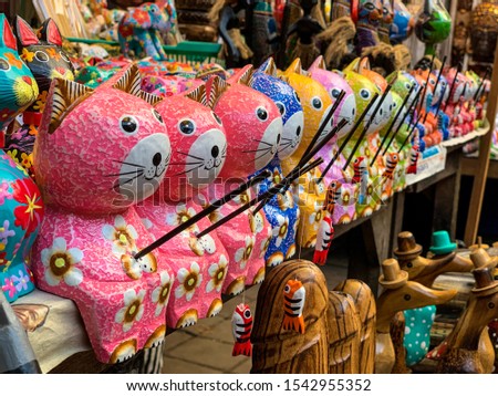 Colorful figures of cats with fishing rods and fish on a hook, cute toys cartoon cats, souvenirs in a shop on Ubud market, Bali