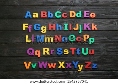 Colorful magnetic letters on black wooden background, flat lay. Alphabetical order