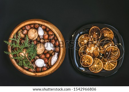  on black table, top view, flat lay. Festive table settin. Wooden bowl with nuts, walnuts and hazelnuts. Dish decorated with Christmas baubles and slices of dried oranges