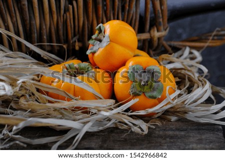 Ripe, juicy persimmon in straw on a wooden table.