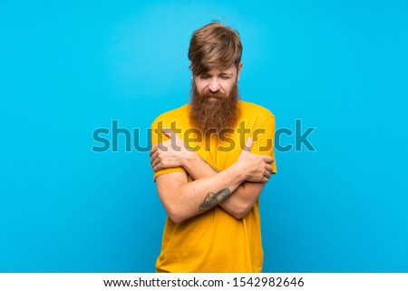 Redhead man with long beard over isolated blue background freezing