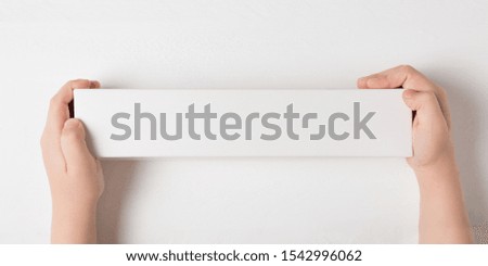 White rectangular cardboard box in children's hands. Top view, white background