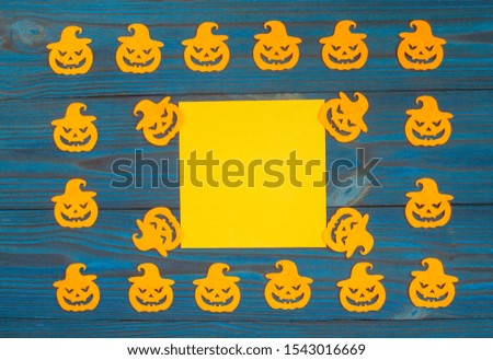 Yellow square sheet of paper on a wooden blue background. Around felt carved orange pumpkins. Halloween background.
