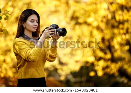beautiful woman photographer with camera takes pictures in park in autumn. copy space