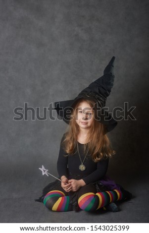 Cute girl wearing black witches hat and multicolour striped tights sitting on the floor looking at camera