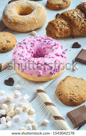 Colorful concept made of sweets. Pink donut with a hole and icing between other sweets on a white wooden background.