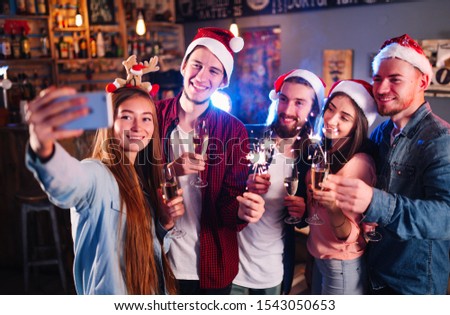Holiday group selfie. Group of young friends having fun at New Year's Eve party and making crazy faces and taking selfies. Group of beautiful young people in Santa hats.