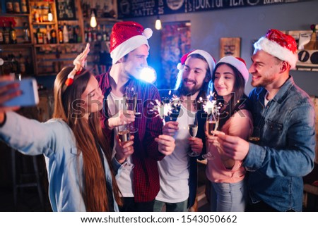 Holiday group selfie. Group of young friends having fun at New Year's Eve party and making crazy faces and taking selfies. Group of beautiful young people in Santa hats.