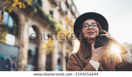 Photographer in glasses with retro photo camera. Tourist portrait. Smiling girl in hat travels in Barcelona holiday. Sunlight flare street in europe city. Traveler hipster shooting architecture, copy