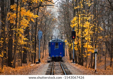 Railroad single track through the woods in autumn. Fall landscape. red stop semaphore signal. Last railway carriage of blue train back view. Royalty-Free Stock Photo #1543067426