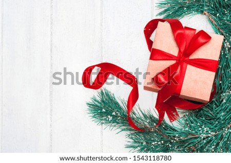 Christmas holiday background, gift with a red ribbon and bow, snow and green pine branches on a white wooden background. Christmas decoration composition