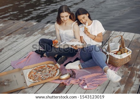 Beautiful girls in a park. Friends sitting near river. Girls eatting pizza