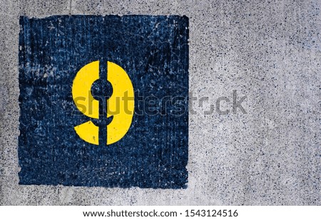 Yellow number 9, nine, in dark blue square, offset on flat concrete surface.