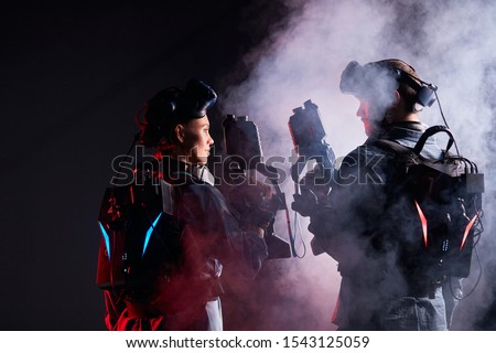 Man and woman stand opposite each other, team in virtual reality game. Isolated over black smoky background