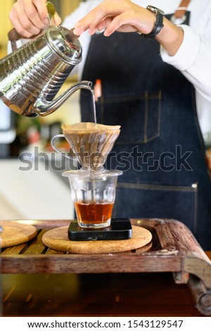 Barista woman girl hot water prepare filtered coffee from silver teapot to beautiful transparent chrome drip maker on white simple weights.Every thick wooden table cafe shop. Steam
