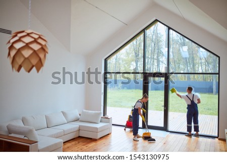 Preparing house for new tenant. Cleaning service washing floor, window. Man cleaning panoramic window with view on garden. Woman sweeping the floor Royalty-Free Stock Photo #1543130975