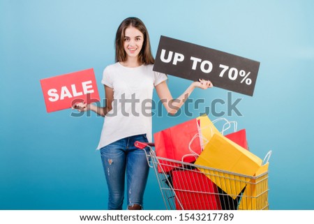 brunette woman with shopping pushcart full of colorful red and yellow paper bags and 70% sale sign isolated over blue